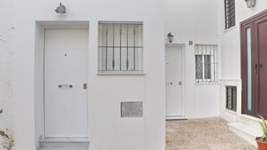 Un edificio blanco con una puerta, una ventana con barrotes y una pequeña señal en la pared.