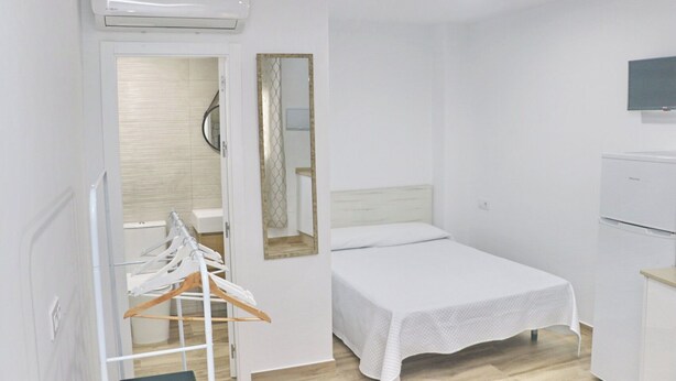 Una habitación pequeña y limpia con una cama, un espejo, un televisor y un armario blanco.