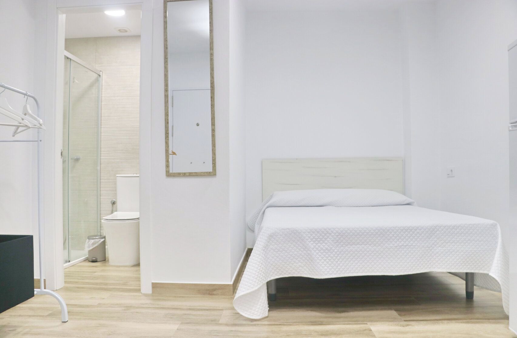 Ein Schlafzimmer mit einem Bett, einem weißen Kopfstück, einem Spiegel und einem Duschbereich.