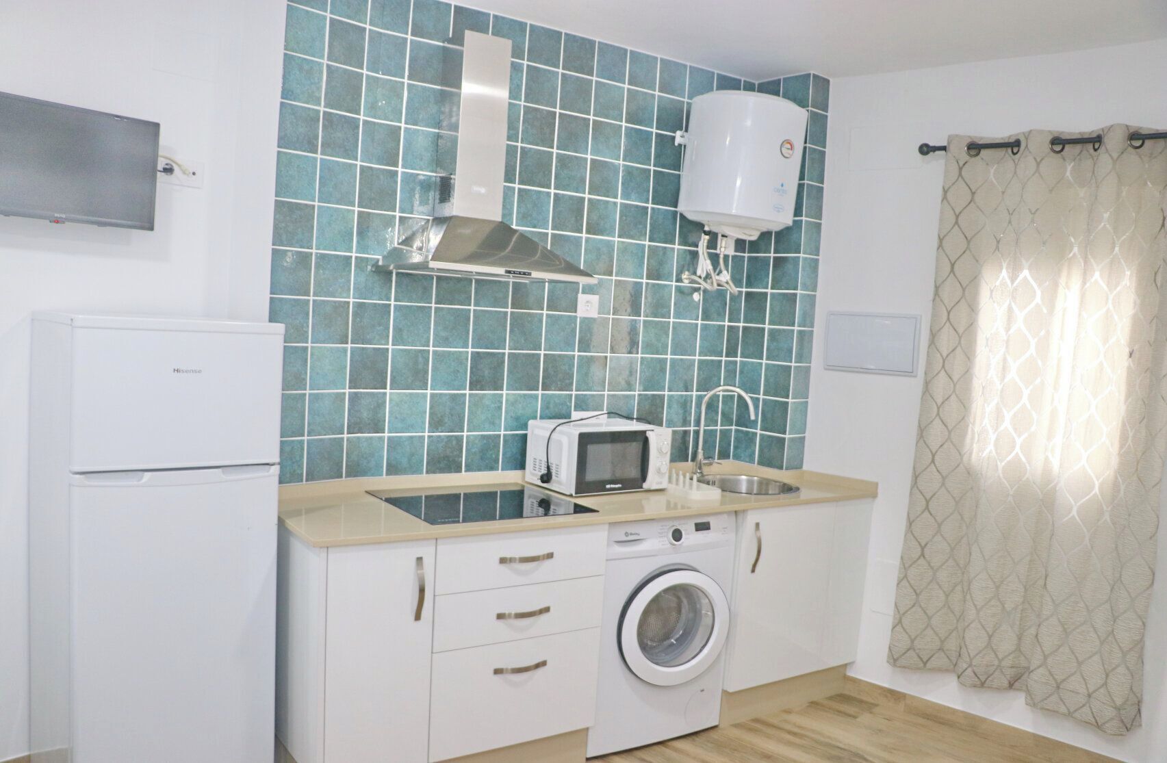 A compact kitchen with a washing machine, a microwave, and a water heater.