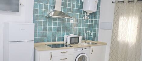 A compact kitchen with a washing machine, a microwave, and a water heater.