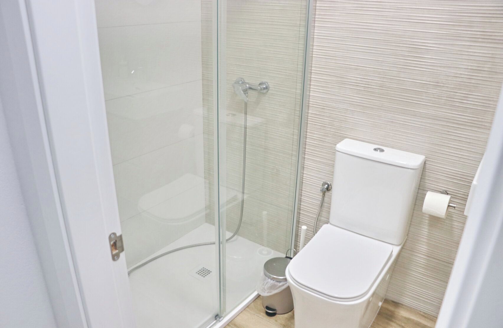 Et moderne badeværelse med en glasbrusekabine, et toilet og en skraldespand.