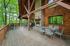 A wooden cabin with a stone fireplace, outdoor seating, and a view of the forest. - Acacia Ridge Lodge | Hocking Hills, 4BR, Hot Tub (Rockbridge)