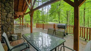 A covered deck with stone walls, outdoor furniture, and a grill.