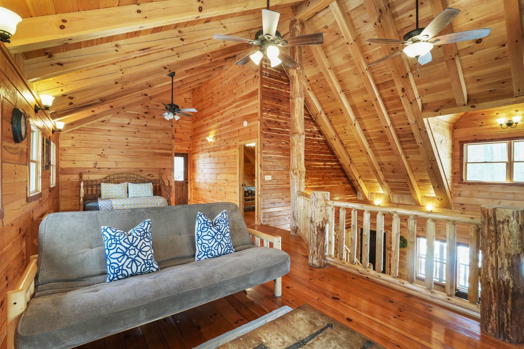 A log cabin interior with a sofa, ceiling fans, and a wooden staircase.
