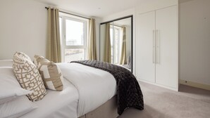 Een moderne slaapkamer met een groot bed, een kledingkast en een raam met gordijnen.