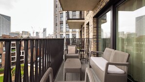 Een balkon met rieten meubilair, uitzicht op de stad en een gevel van een bakstenen gebouw.