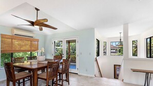 A dining area with a wooden table and chairs, a ceiling fan, and a view of the outdoors.