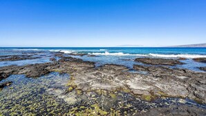 A rocky shoreline with clear blue water and distant land.