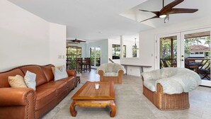 A spacious living area with a brown leather sofa, wicker chairs, and a wooden coffee table.