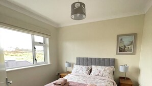 Un dormitorio con una cama, dos mesitas de noche, una ventana y un cuadro en la pared.