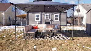 A covered outdoor seating area with a sectional sofa and a patterned rug. - Game Room Retreat with Firepit + Gym + Sleeps 12 (Indianapolis)