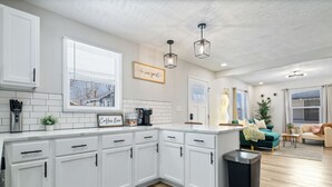 A modern kitchen with white cabinets, a coffee bar, and a view of the city. - Game Room Retreat with Firepit + Gym + Sleeps 12 (Indianapolis)