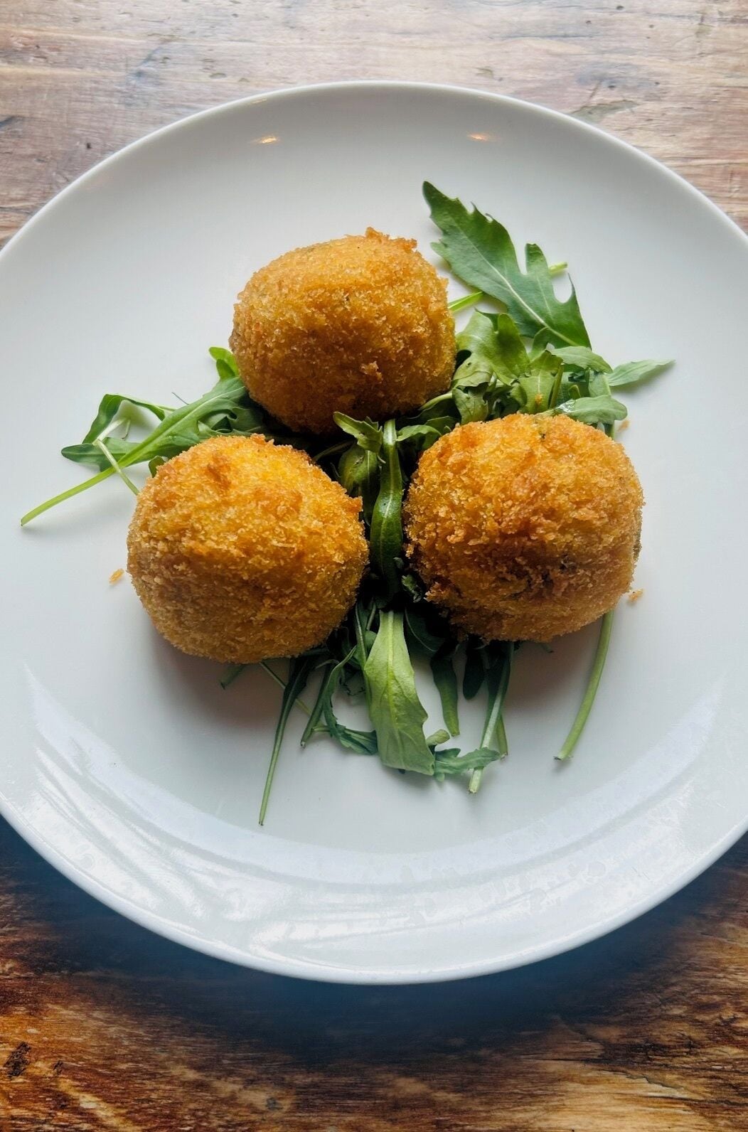 A plate with four golden-brown croquettes and some green salad leaves.