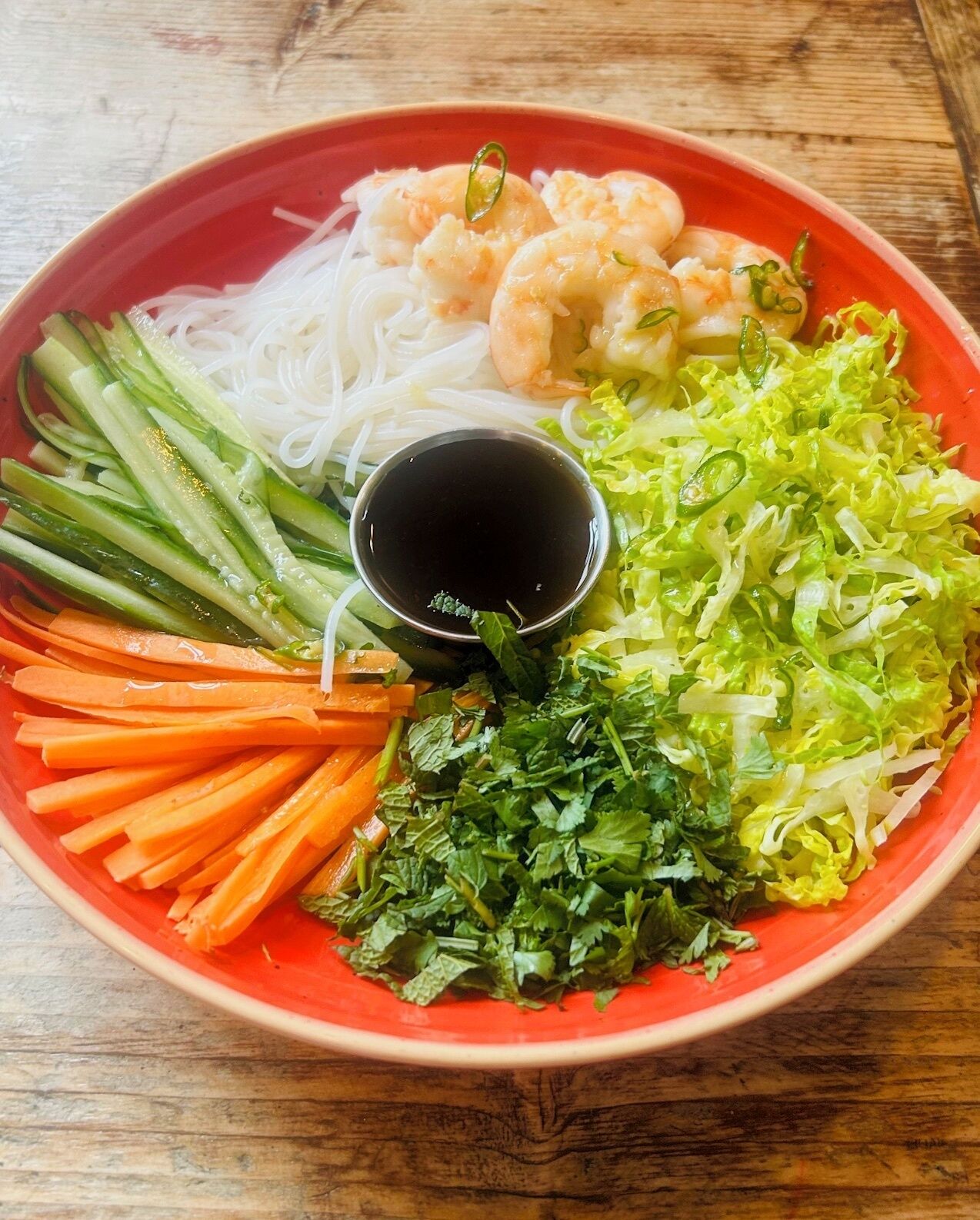 Un tazón de sopa de fideos vietnamita con camarones, fideos, verduras y un recipiente pequeño para salsa.