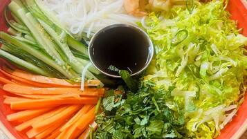 Un tazón de sopa de fideos vietnamita con camarones, fideos, verduras y un recipiente pequeño para salsa.