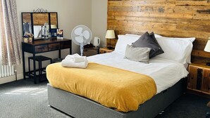 A modern hotel room with a large bed, a wooden headboard, a desk with a mirror, a fan, and a lamp. - The Brookmill (London)