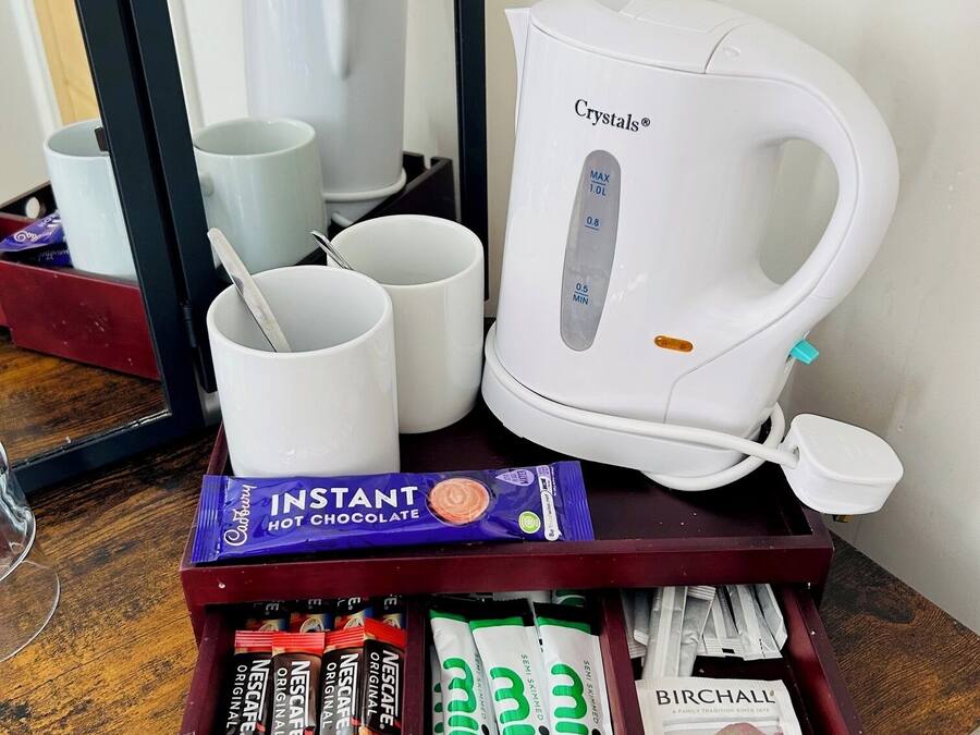 Een koffiezetapparaat, verschillende kopjes, een schaal met snacks en een boek op een houten tafel.