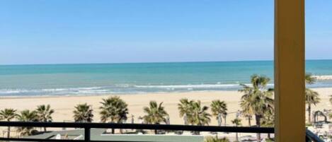 A balcony with a view of the beach and palm trees.