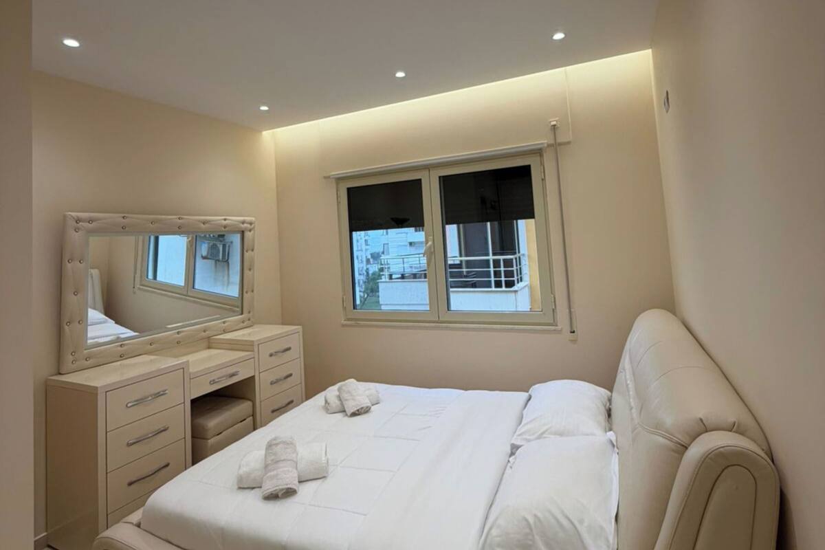 Un dormitorio con cama, cómoda, espejo, ventana y lámpara en el techo.