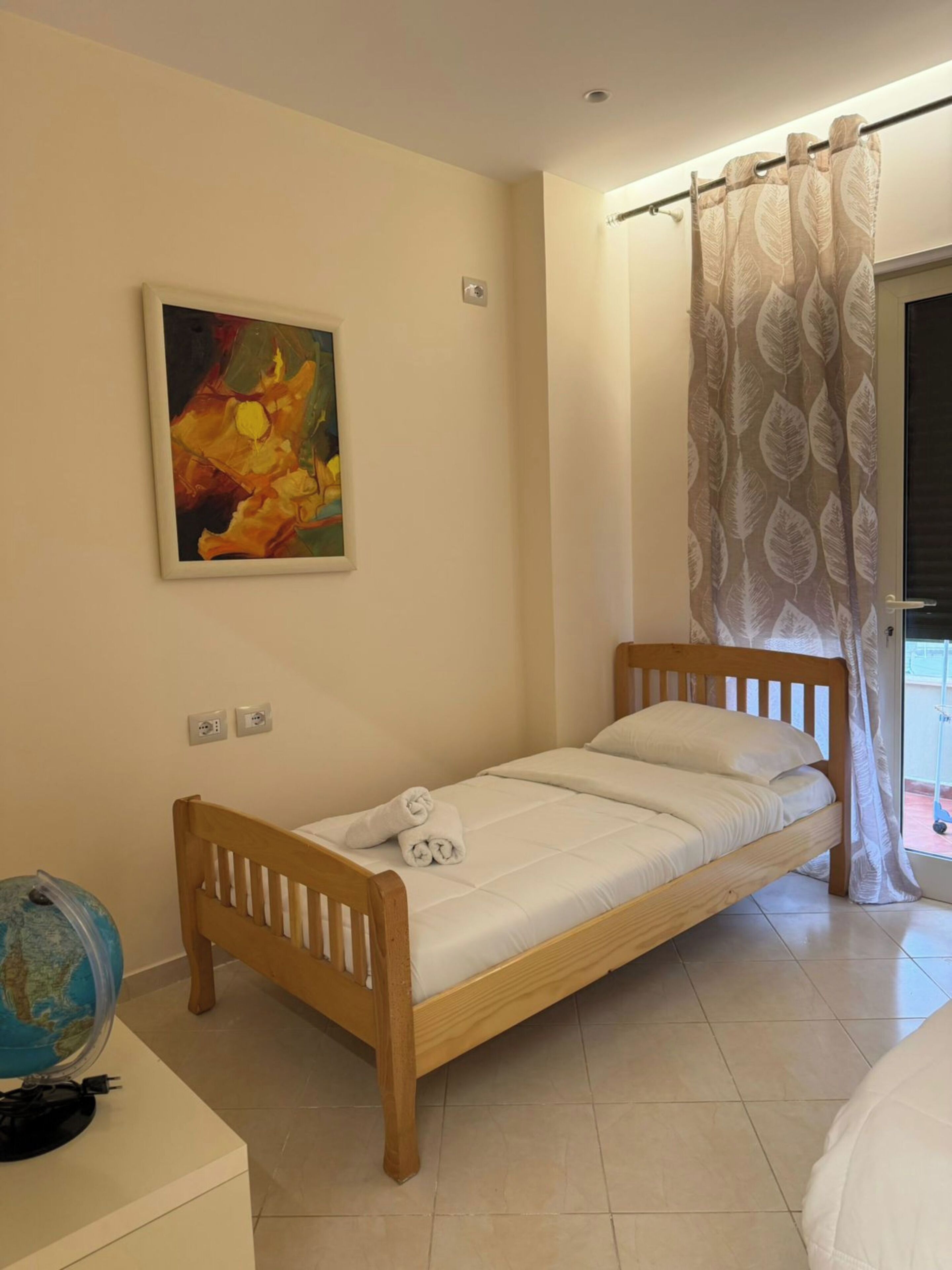 A single bed with a wooden frame, a globe on a side table, and a painting on the wall.