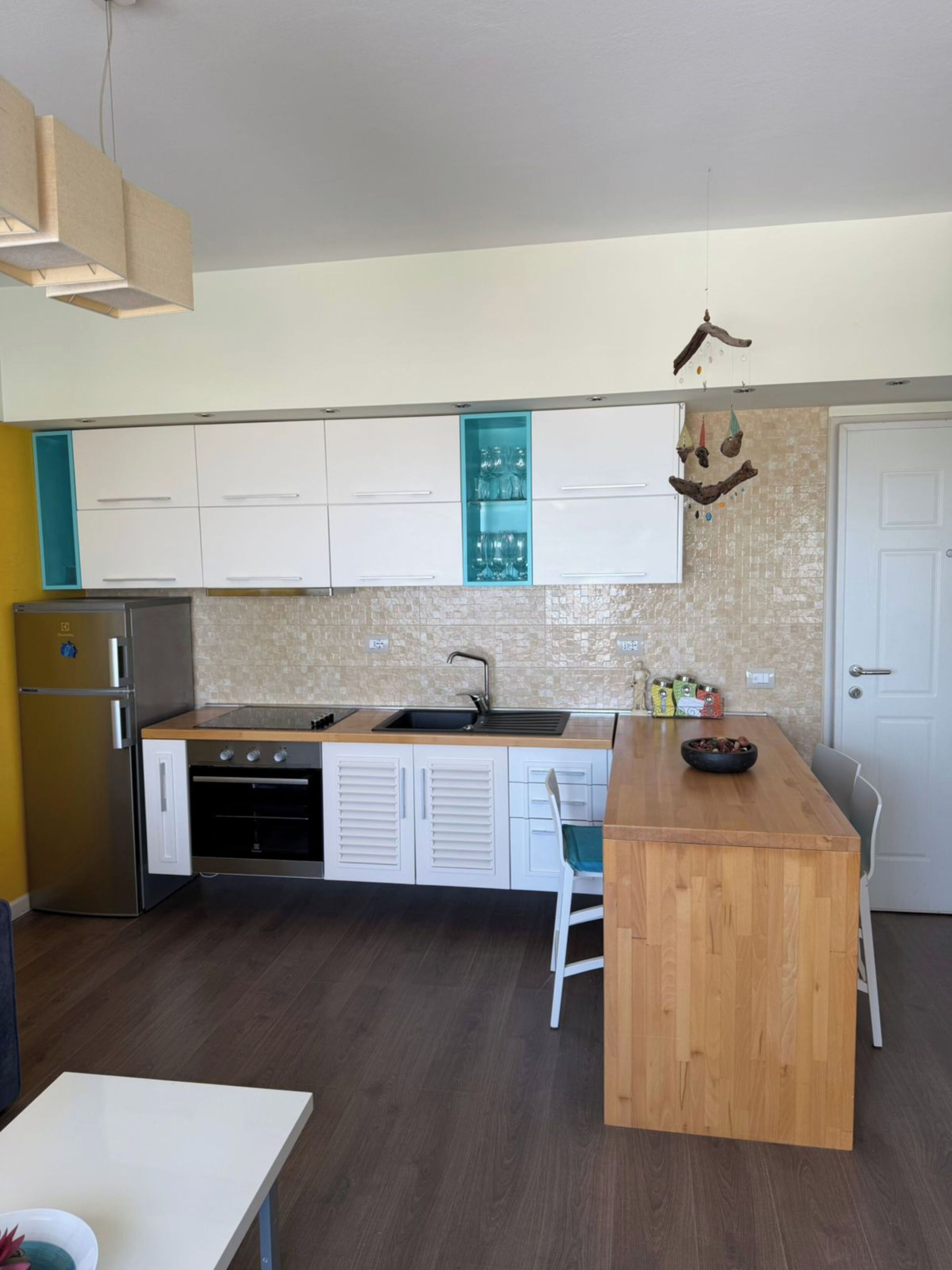 A compact kitchen with white cabinets, a wooden island, a built-in sink, and a refrigerator.