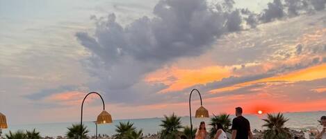Un restaurant doté d’une terrasse offrant une vue sur la mer, avec des tables et des chaises rondes, et d’où l’on peut admirer le coucher du soleil.