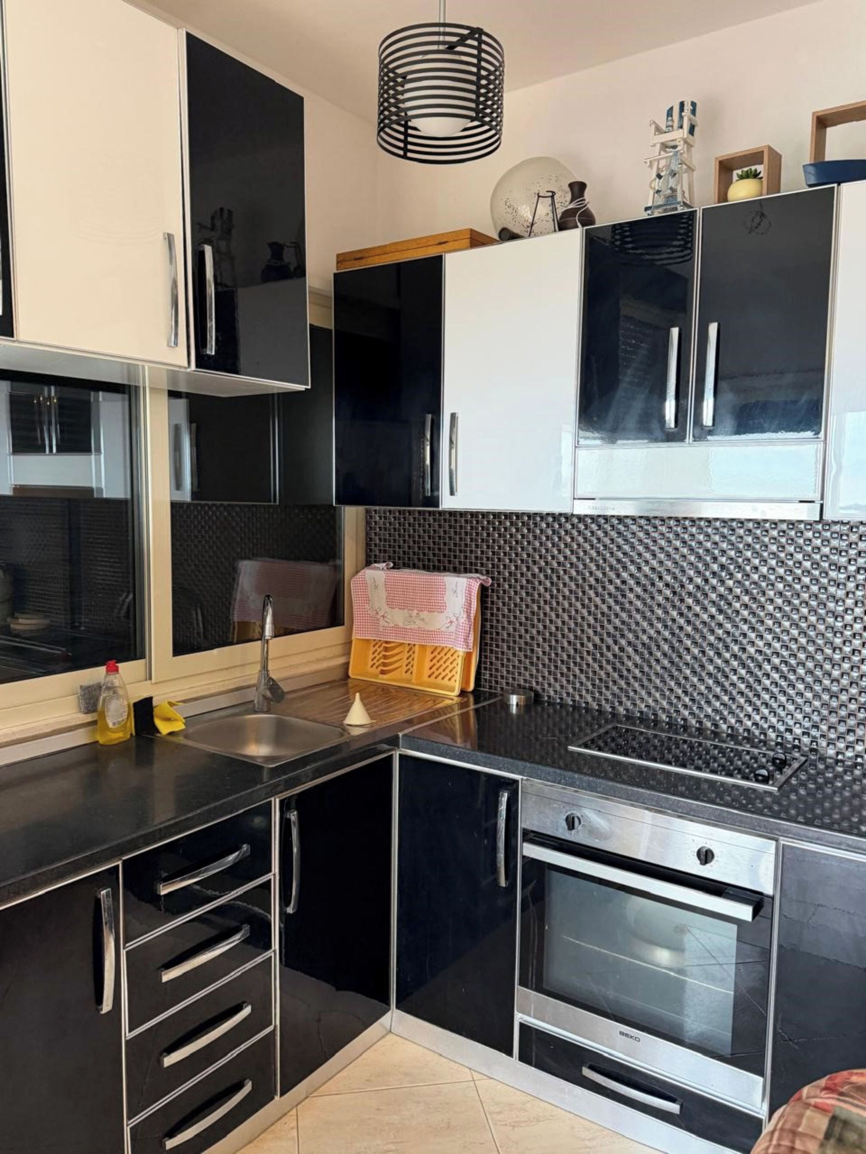 A modern kitchen with black cabinets, a stainless steel sink, a built-in oven, and a patterned backsplash.