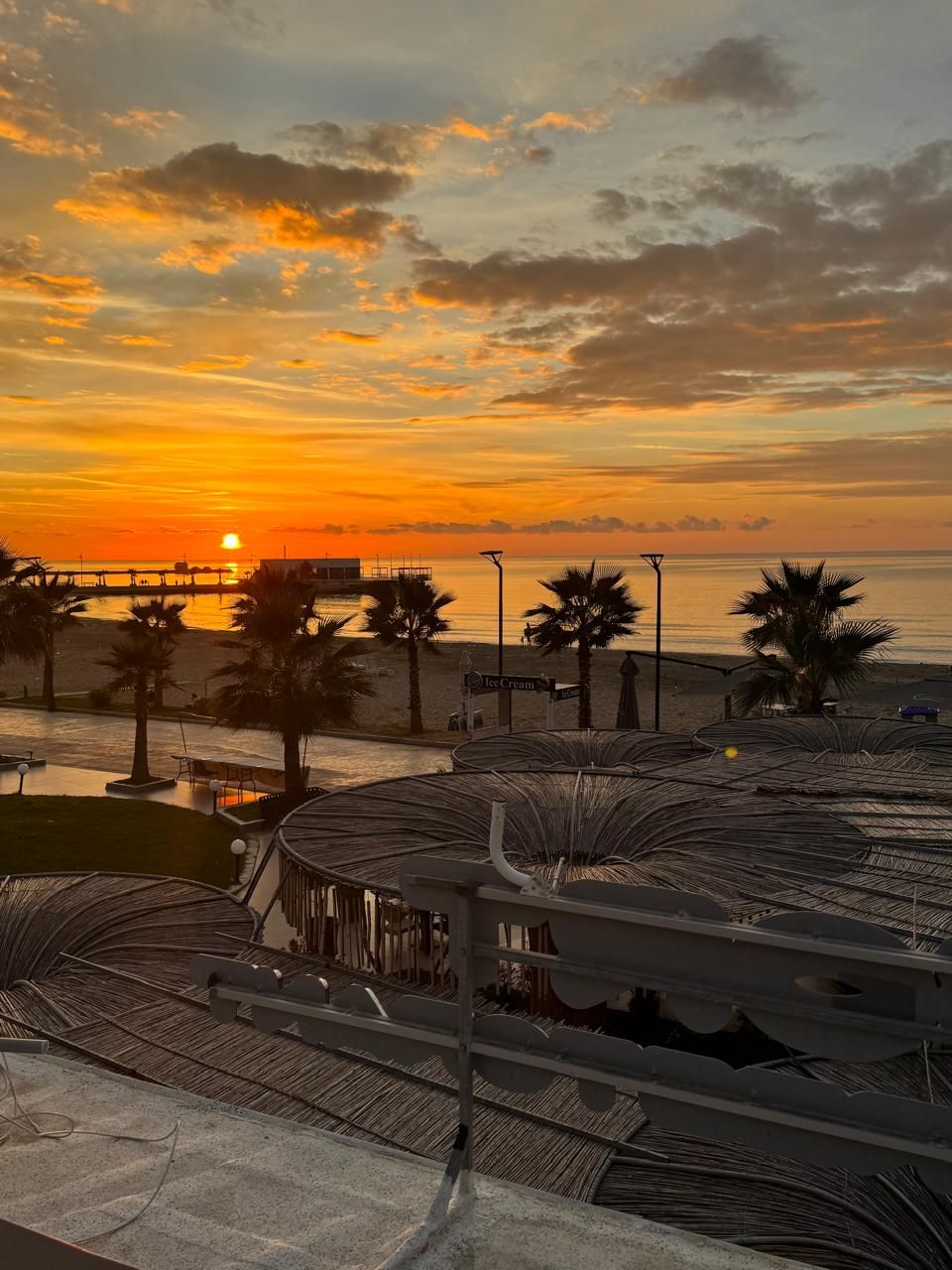 A beachside view with a sunset, palm trees, and a pier.