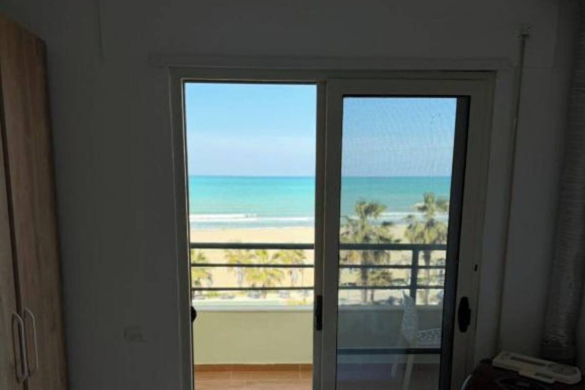 Una habitación con cama, armario y puerta corrediza de vidrio que da a un balcón con vista a la playa.