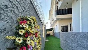 A narrow corridor with a green artificial lawn and a wall adorned with a variety of colorful flowers. - Clarus Apartments (Ibadan)