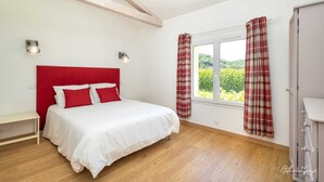 Une chambre à coucher avec un lit blanc, une tête de lit rouge et des rideaux à carreaux.