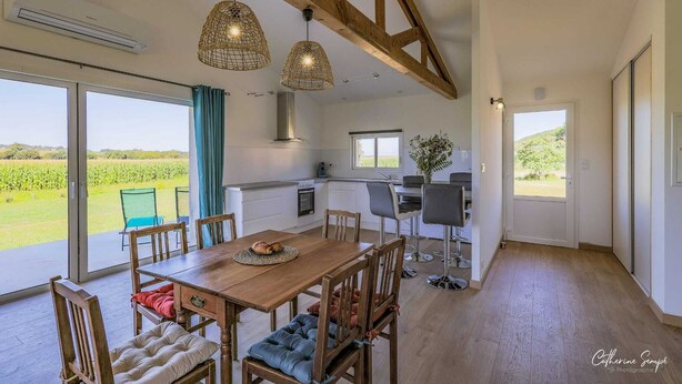 Un vaste espace de salle à manger avec une table et des chaises en bois, une cuisine dotée d’une grande fenêtre et une vue sur un paysage verdoyant.