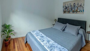A bedroom with a bed, a potted plant, a painting on the wall, and a wooden floor. - MOT Nicaragua 5800 (Buenos Aires)