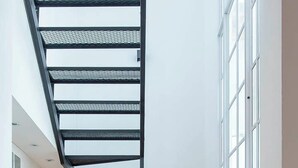A modern staircase with a black metal railing, a wooden chair, and a small table with shelves. - MOT Nicaragua 5800 (Buenos Aires)