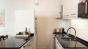 A compact kitchen with a black countertop, white cabinets, a stainless steel sink, and a hanging light fixture.