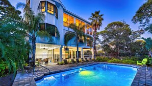 A two-story building with a swimming pool, outdoor seating, and palm trees. - Prince of Tides - 6 BEDROOM with POOL+ELEVATOR - SHORT WALK TO BEACH (Eastpoint)