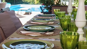 Une table à manger dressée avec de l’assiette verte, des serviettes blanches et de la verrerie verte, avec une piscine et du mobilier d’extérieur en arrière-plan.