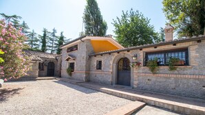 Un bâtiment en pierre avec un toit en tuiles, une cour en gravier et un petit jardin agrémenté de fleurs roses.