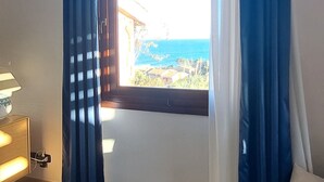 Una habitación con vista al mar, una ventana con cortinas azules, una lámpara y suelo de baldosas.