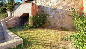 Una casa de piedra con un porche cubierto, una pequeña escalera y un jardín con césped.