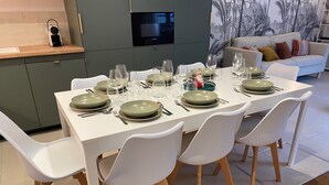 Un área de comedor moderna con una mesa blanca dispuesta para seis personas, rodeada de sillas blancas con patas de madera.