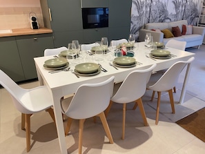 A modern dining area with a white table set for six, surrounded by white chairs with wooden legs.