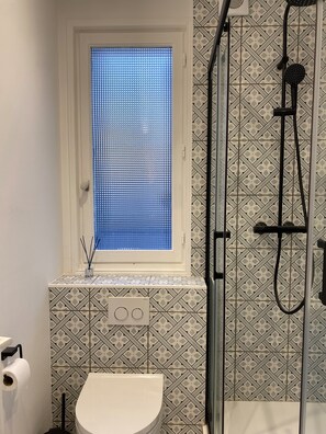 A bathroom with a toilet, a shower, and a window with blinds.