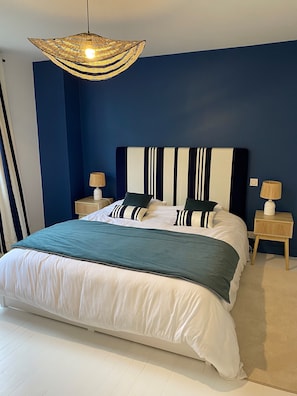 A neatly made bed with a striped headboard, two bedside tables with lamps, and a hanging light fixture.