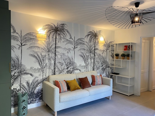 A living room with a light grey sofa, patterned wall, and a white shelving unit.