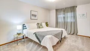 Un dormitorio con cama, una mesita de noche con lámpara y una ventana con cortinas.