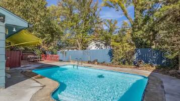 Uma piscina retangular com borda curva, rodeada por um deck de concreto e cerca de madeira.
