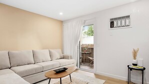 Ein modernes Wohnzimmer mit einem beigefarbenen Sofa, einem Holztisch und einem kleinen schwarzen Beistelltisch mit einer Vase und Büchern.
