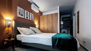 A modern bedroom with a bed, bedside lamp, wall-mounted air conditioner, and a small table with a plant.